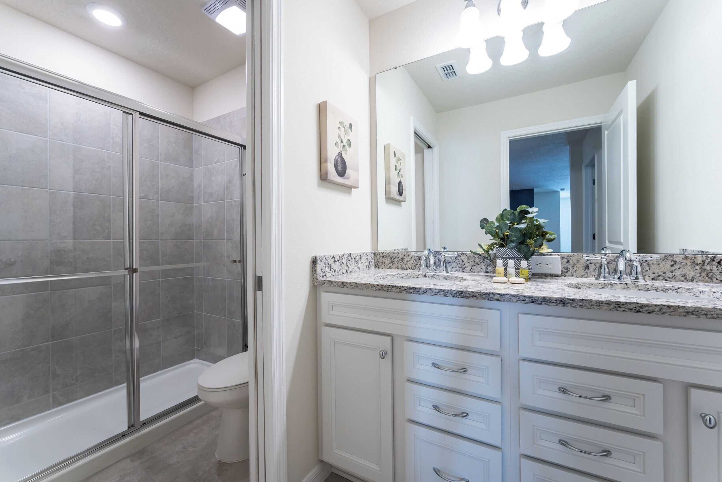 Une salle de bain moderne dotée d’une douche à parois de verre, de toilettes blanches et d’un meuble-lavabo avec un plan de travail en granit et plusieurs tiroirs.