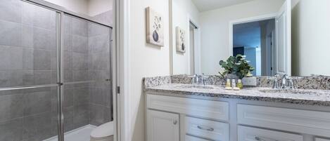 Une salle de bain moderne dotée d’une douche à parois de verre, de toilettes blanches et d’un meuble-lavabo avec un plan de travail en granit et plusieurs tiroirs.