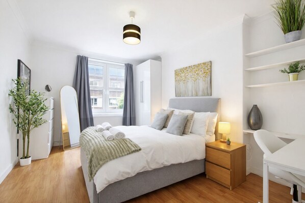 Une chambre à coucher moderne avec un lit, des tables de chevet, un bureau et une plante en pot.