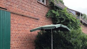Un patio al aire libre con un muro de ladrillo, un paraguas verde y dos sillas de mimbre.