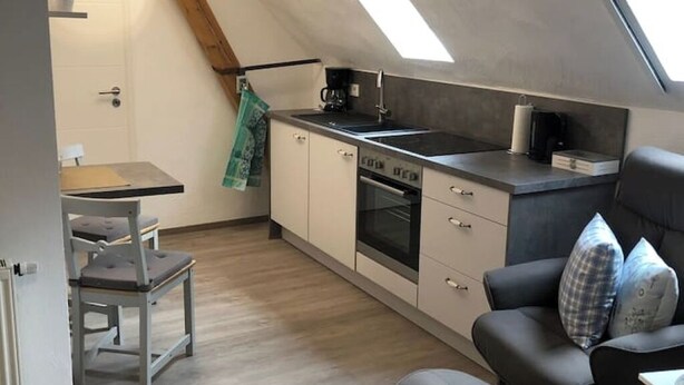 Una cocina compacta con tragaluz, un comedor con mesa y sillas, y un sofá con cojines.
