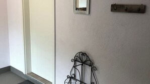 Un rincón de una habitación con pared blanca, un espejo pequeño y un adorno metálico.