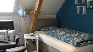Un dormitorio con una cama, una silla, una mesita y una lámpara de pie.