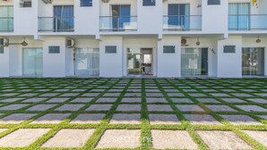 A multi-story building with a flat roof, large windows, and a paved courtyard with grass inlays. - Elegant Duplex w Sw. Pool 280m fr the Beach Prm007 (Santa Cruz Cabralia)