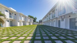 A modern building with a courtyard featuring a patterned lawn and a clear sky. - Elegant Duplex w Sw. Pool 280m fr the Beach Prm007 (Santa Cruz Cabralia)