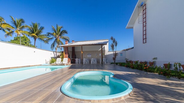 A swimming pool area with lounge chairs, a covered seating area, and a building with a tiled roof. - Elegant Duplex w Sw. Pool 280m fr the Beach Prm007 (Santa Cruz Cabralia)