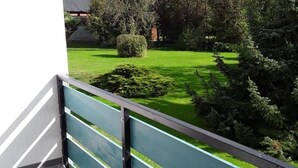 En balkon med udsigt over en velplejet have, med græsplæne og forskellige buske.