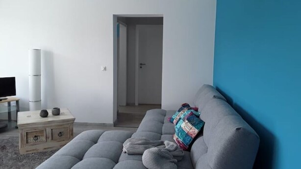 En moderne stue med en grå sofa, et lille træsidebord og en blå væg.