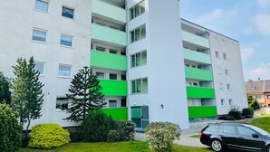 En moderne, høj beboelsesejendom med flad facade, altaner og en bil parkeret i indkørslen.
