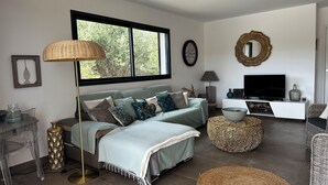 Ein modernes Wohnzimmer mit Sofa, Fernseher, Lampe und einem großen Fenster.