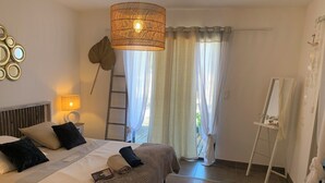 Ein Schlafzimmer mit Bett, Nachttischlampe und Blick ins Freie durch leichte Vorhänge.