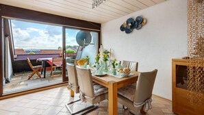 Ein Essbereich mit Tisch für vier Personen, eine Schiebetür zu einem Balkon und einem dekorativen Wandbild.