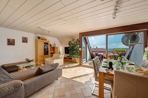 A modern living room with a sofa, dining table, and a view of the sea through large windows.