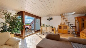 Ein großzügiger Wohnbereich mit einer Glastür zum Balkon, einem Holzesstisch und einer Treppe.