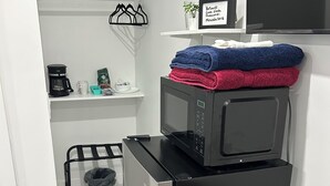 A compact kitchen with a refrigerator, microwave, and coffee maker. There is a small shelf with towels and a framed picture. - Beautiful Private Room, Near the AirPort - Free Parking (Miami)