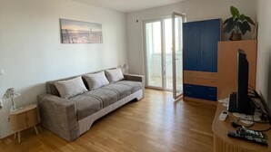 A living room with a grey sofa, wooden flooring, a painting on the wall, a cabinet, and a TV stand with remote controls. - Charming 1-bedroom apartment in delightful Split with AC (Split)