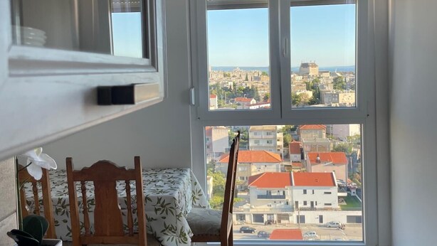 A room with a large window offering a city view, a wooden chair, a small table, and a potted plant. - Charming 1-bedroom apartment in delightful Split with AC (Split)