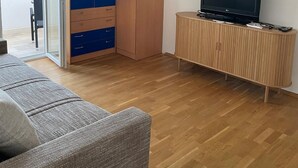 A modern living room with a sofa, a TV on a wooden cabinet, and a wardrobe with a plant on top. - Charming 1-bedroom apartment in delightful Split with AC (Split)