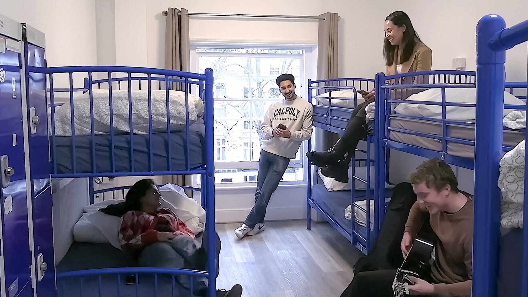 Une chambre de dortoir avec des lits superposés, une fenêtre avec des rideaux et une vue sur l’extérieur.