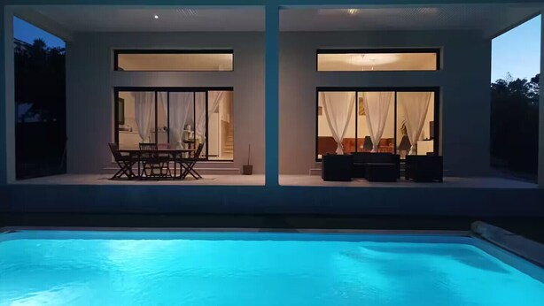 Une maison moderne dotée d’une piscine, de grandes fenêtres et d’un espace salon extérieur.