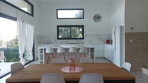 Une cuisine moderne avec des meubles blancs, une table à manger en bois et une grande fenêtre.