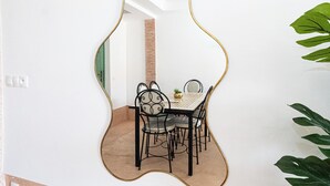 Een eetgedeelte met een tafel en stoelen, een hangspiegel en een bakstenen muur op de achtergrond.