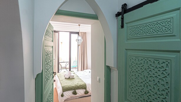 Een gang die leidt naar een slaapkamer met een bed, een kroonluchter en uitzicht op de omgeving.