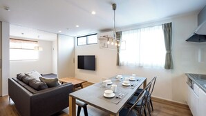 Una sala de estar moderna con un sofá, una mesa de comedor preparada para cuatro personas y un televisor montado en la pared.