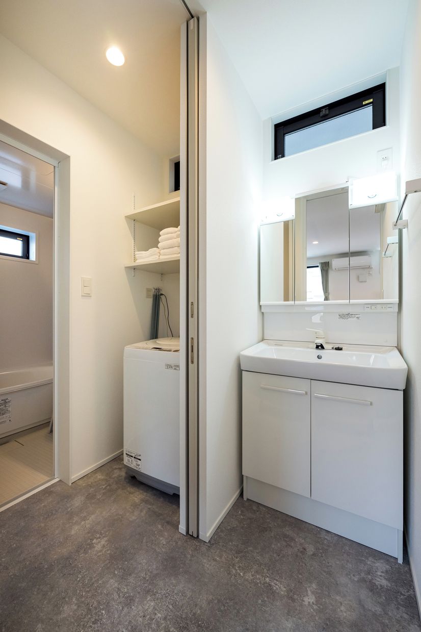 Un baño moderno con lavadora integrada, un lavabo con espejo y un perchero para toallas.