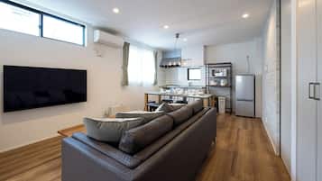 A modern living room with a large flat-screen TV, a sofa, and a dining area with a table and chairs.