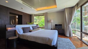 A modern bedroom with a large bed, a TV, and a view of greenery outside. - Luaana@CasaVela - 2BR Apartment with Ocean View (Koh Samui)