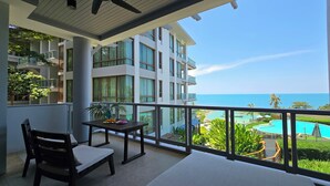A balcony with a table and chairs, overlooking a pool and a building with multiple floors and balconies. - Luaana@CasaVela - 2BR Apartment with Ocean View (Koh Samui)