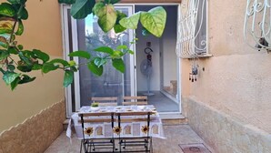 Un patio con una mesa lista para dos personas, un extintor y una ventana con reja de metal.