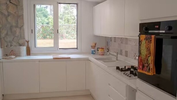Una cocina moderna con armarios blancos, una pared de acento de piedra, un ventanal grande y un horno empotrado.