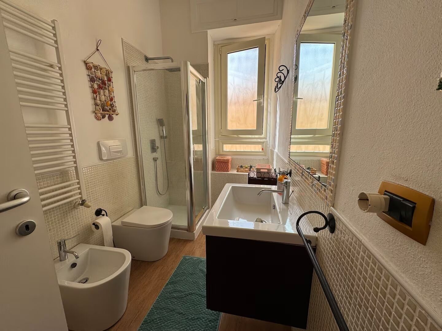 A bathroom with a shower, toilet, bidet, sink, and a large mirror.