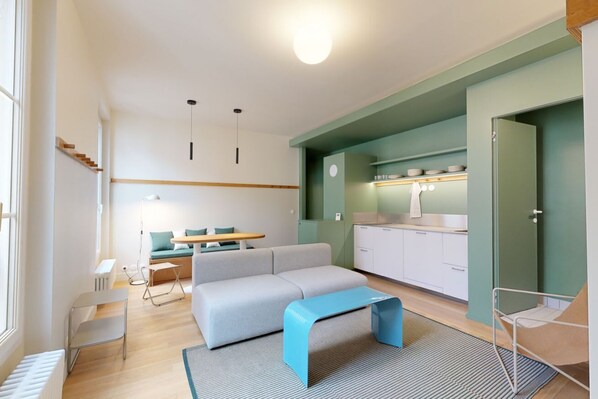 A modern living room with a sofa, a coffee table, a dining area with a table and chairs, and a kitchen area with cabinets and a countertop. - A400 JOIVY Charming 2-bed flat w/ shared spaces (Paris)