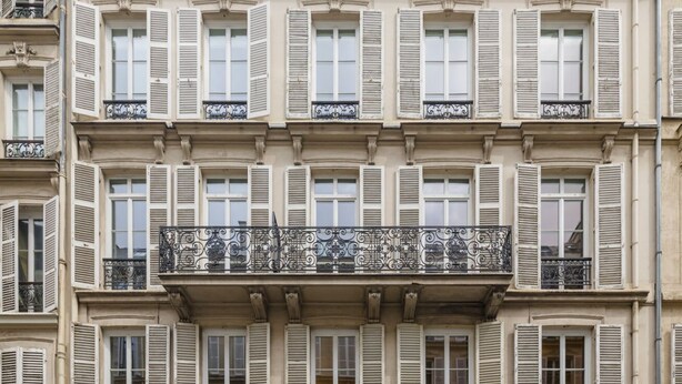 A multi-story building with uniform window shutters and ornate balcony railings. - JOIVY Pleasant 1-bed flat w/ shared courtyard (Paris)