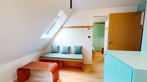 A room with a sloped ceiling, a bench with cushions, a small table, and a wardrobe. - JOIVY 10 Douai 1BR Velux (Paris)