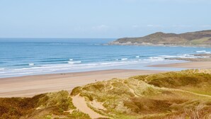 Un paysage côtier avec une plage de sable, des dunes herbeuses et une vue dégagée sur l’océan.