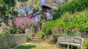 Un sentier de jardin menant à une maison entourée d’une clôture en bois et agrémentée d’un banc.