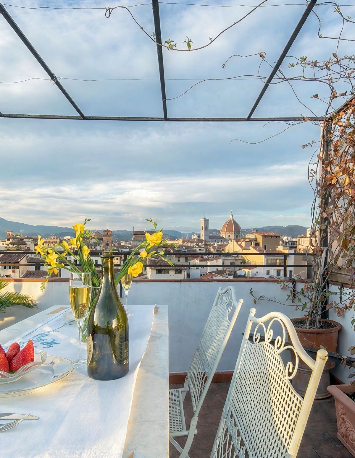 Une table dressée avec une bouteille, des verres et des fraises, donnant sur un paysage urbain avec un bâtiment en forme de dôme.