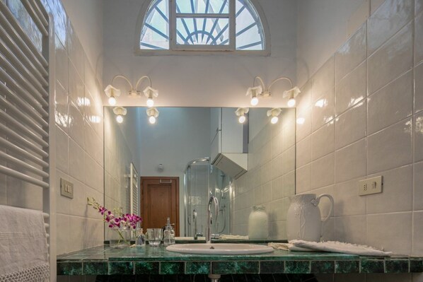 Un baño con un espejo grande, una ducha y un lavabo con un florero.