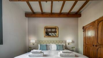 Une chambre avec un grand lit, des poutres apparentes en bois au plafond, un miroir et une armoire.