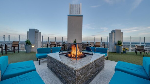 A rooftop terrace with a fire pit, blue seating, and a view of the city skyline.