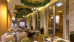 A restaurant with indoor seating, large windows, and hanging greenery. - Ace of Hua Hin Resort - One Bedroom Ace Seaview Suite Private Pool (Cha-am)