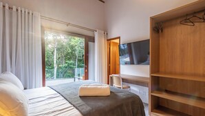 A bedroom with a bed, a TV, a wooden wardrobe, and a balcony with a view of trees. - House w/ Pool 900m From the Beach, Arraial Ptg0030 (Porto Seguro)
