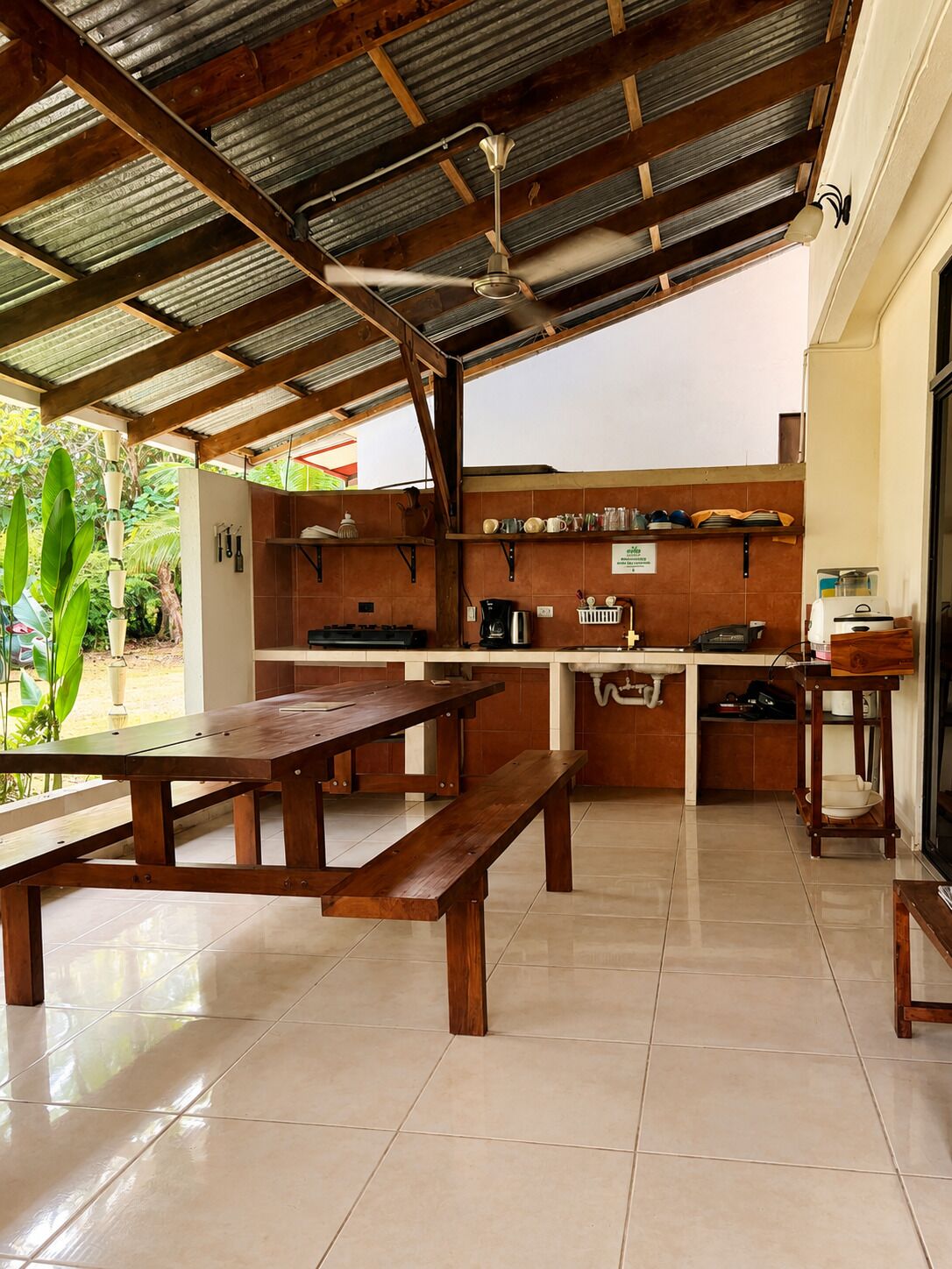 A covered outdoor kitchen with wooden benches, a gas stove, and a coffee maker.