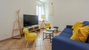 A living room with a TV, yellow chairs, a blue sofa, and a small table. - "La maison du bonheur" (Bois-le-Roi)