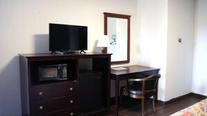 A compact room with a dark wooden desk, a television, a small refrigerator, a chair, and a mirror on the wall. - Hotel O (Oskaloosa)
