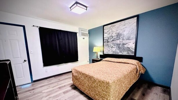A bedroom with a bed, a window with curtains, a wall-mounted air conditioner, and a framed picture. - Hotel O (Oskaloosa)